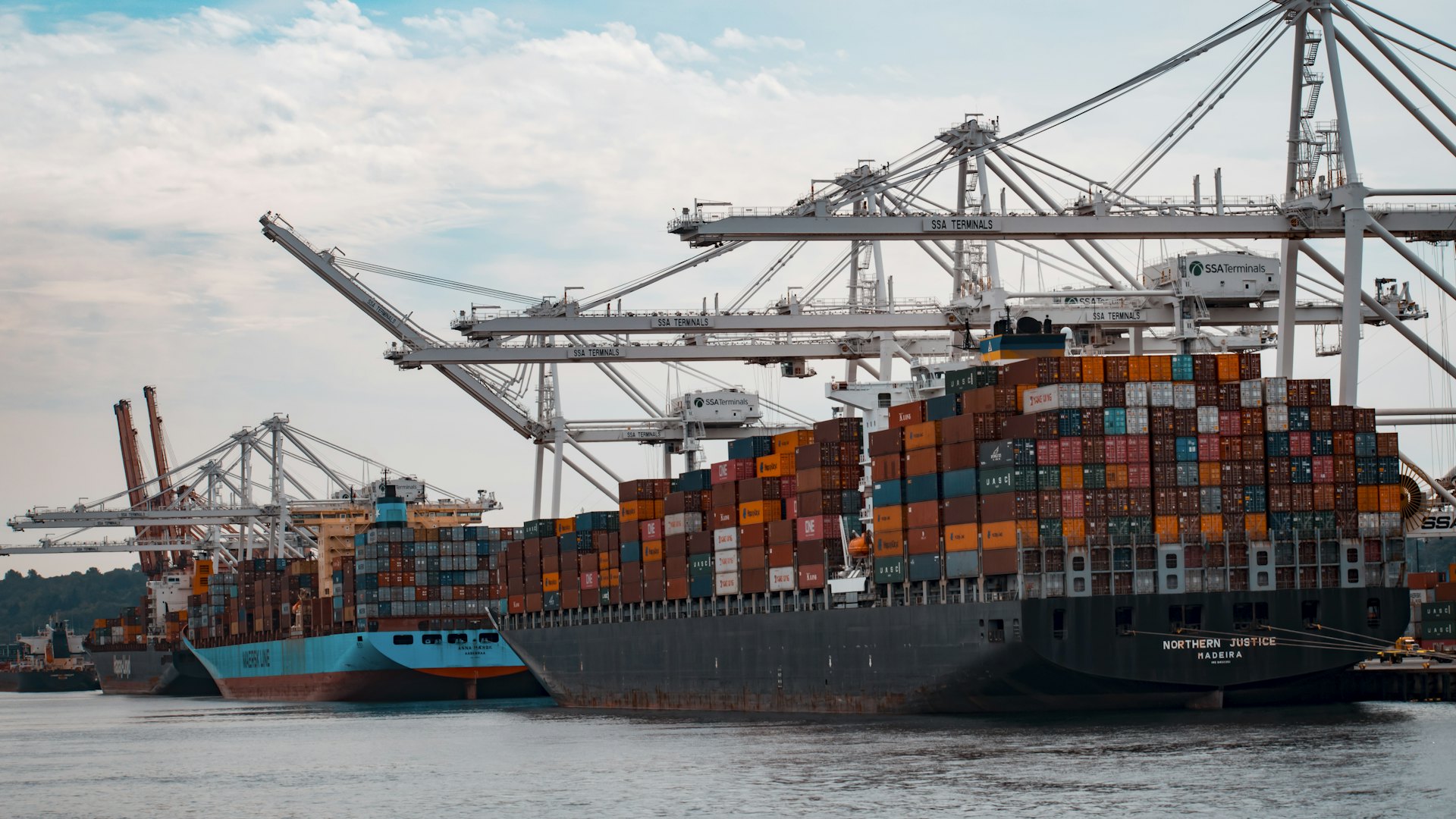 A container ship leaving an international port at sunset.